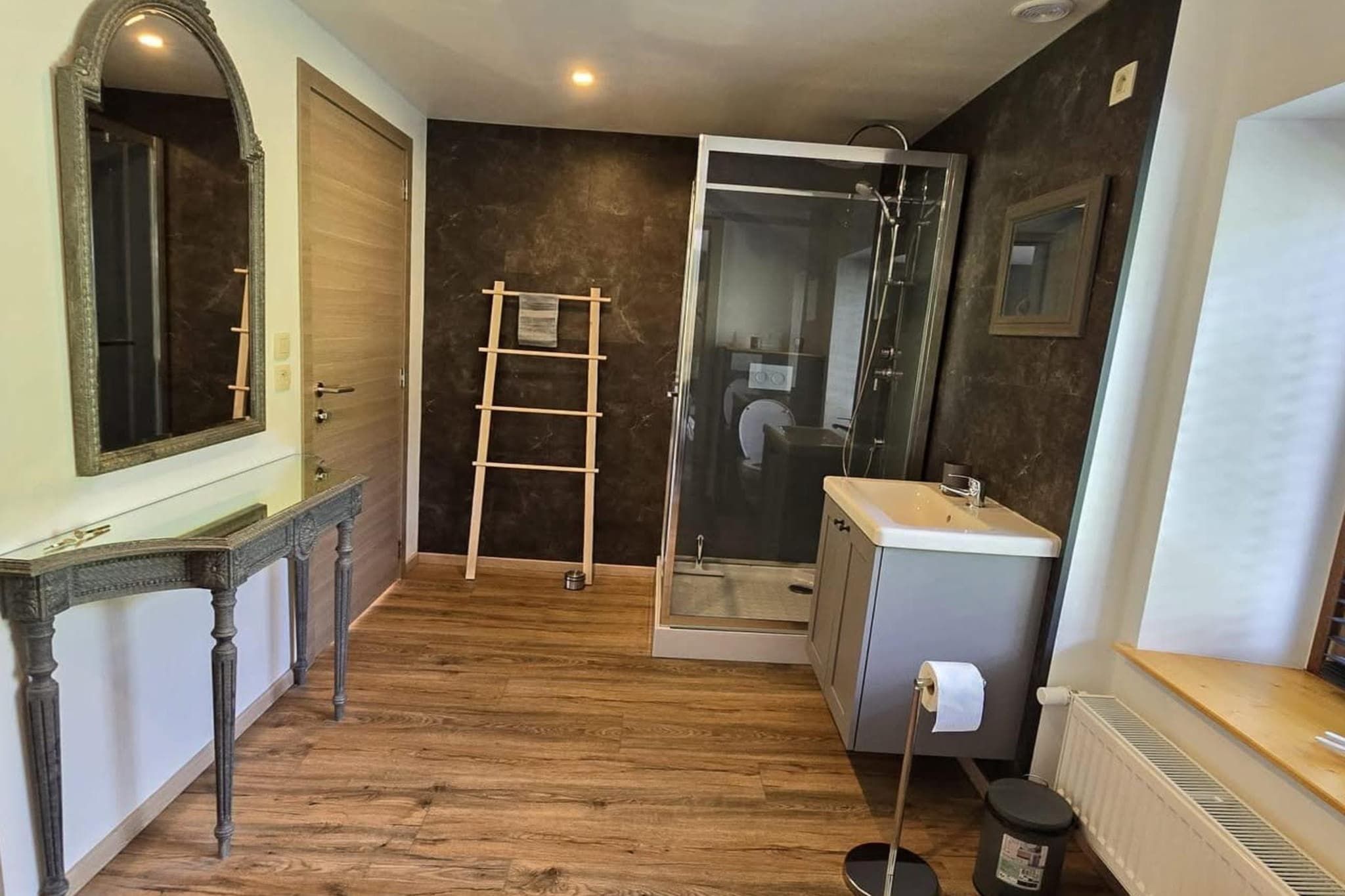 A bathroom with a wooden floor, a glass shower enclosure, a sink, and a mirror.