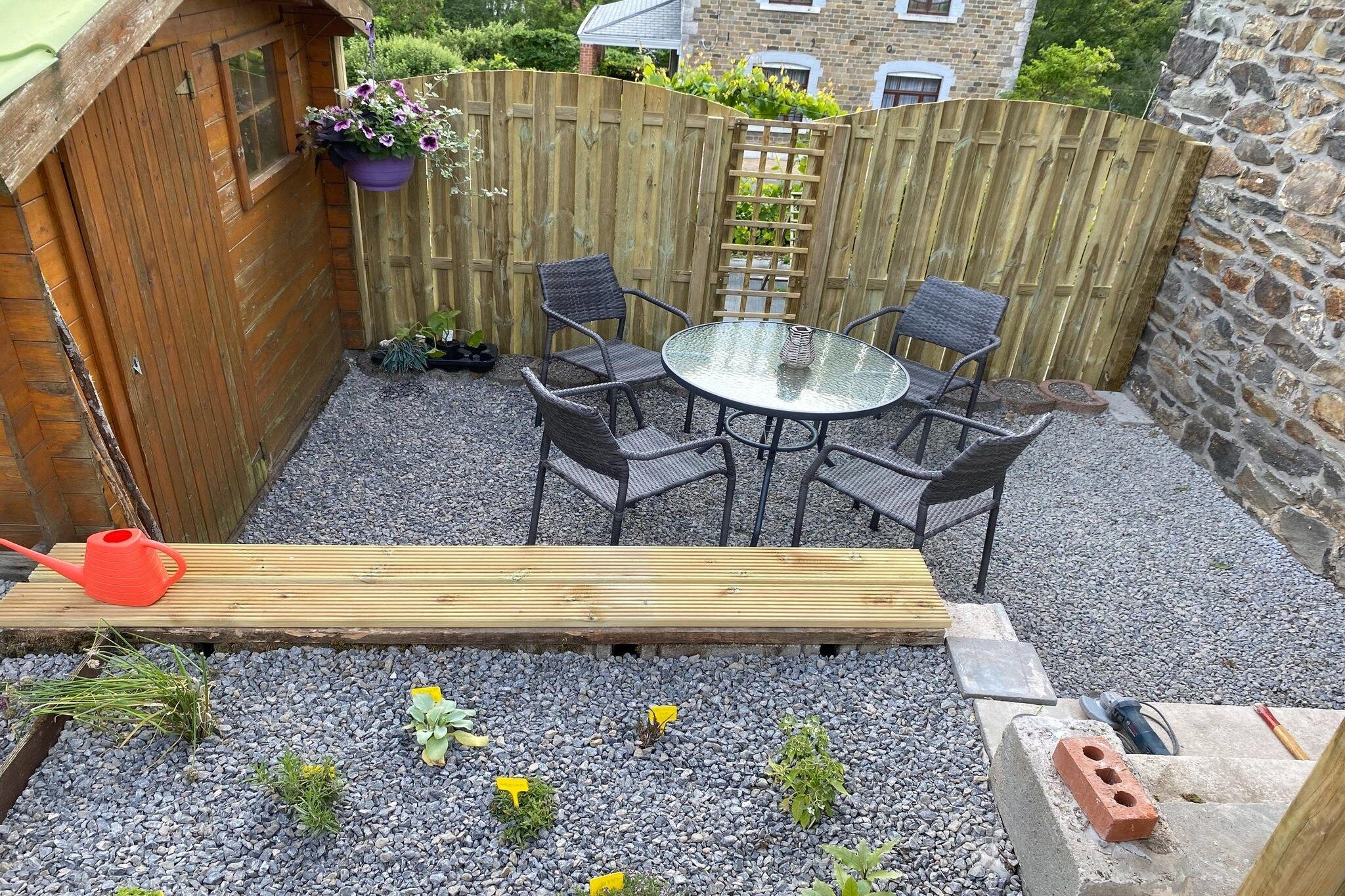 Un patio con un tavolo rotondo in vetro e quattro sedie, circondato da una recinzione in legno e un muro in pietra.
