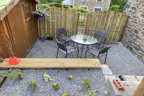 Un patio con una mesa de vidrio redonda y cuatro sillas, rodeado por un cerco de madera y un muro de piedra.