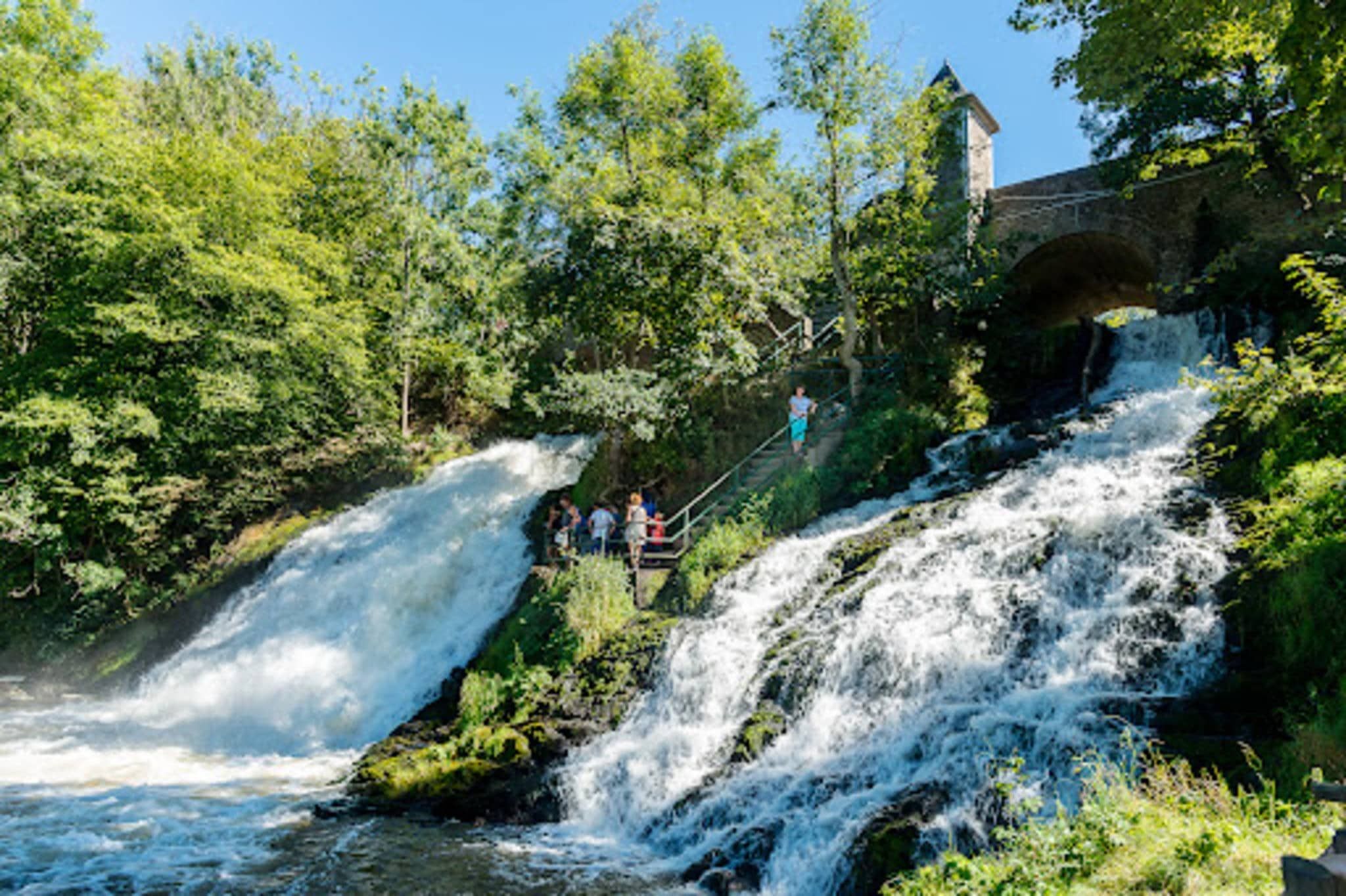 Una cascada amb un pont i una construcció de pedra al fons.