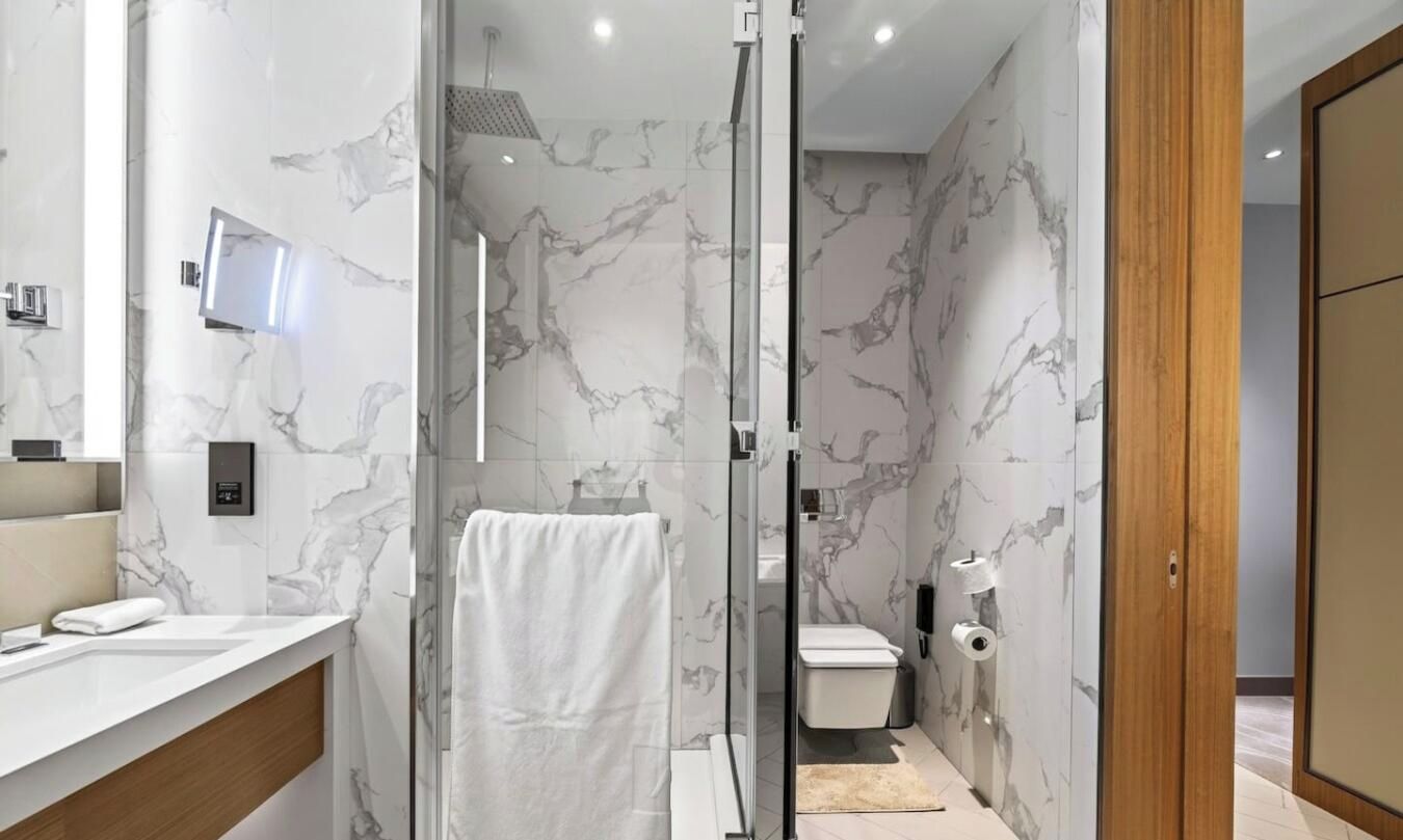 Un baño moderno con cabina de ducha de vidrio, inodoro y lavamanos con faldón de mármol.