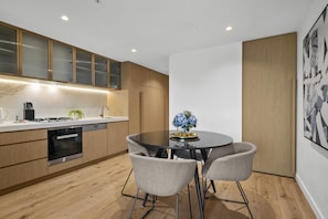 Een moderne keuken met houten kastjes, een inbouwoven en een eethoek met een ronde tafel en stoelen.