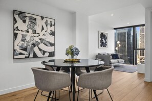 Een moderne woonruimte met een ronde eettafel, grijs gestoffeerde stoelen, een vaas met bloemen en abstracte kunst aan de muren.