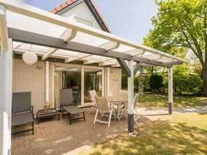 A covered patio area with outdoor furniture, a brick wall, and a glass door leading to an interior space. - Holiday Home in Renesse With Swimming Pool (Renesse)