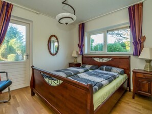 A bedroom with a wooden bed, two bedside tables, a mirror, and a window with curtains. - Holiday Home in Renesse With Swimming Pool (Renesse)