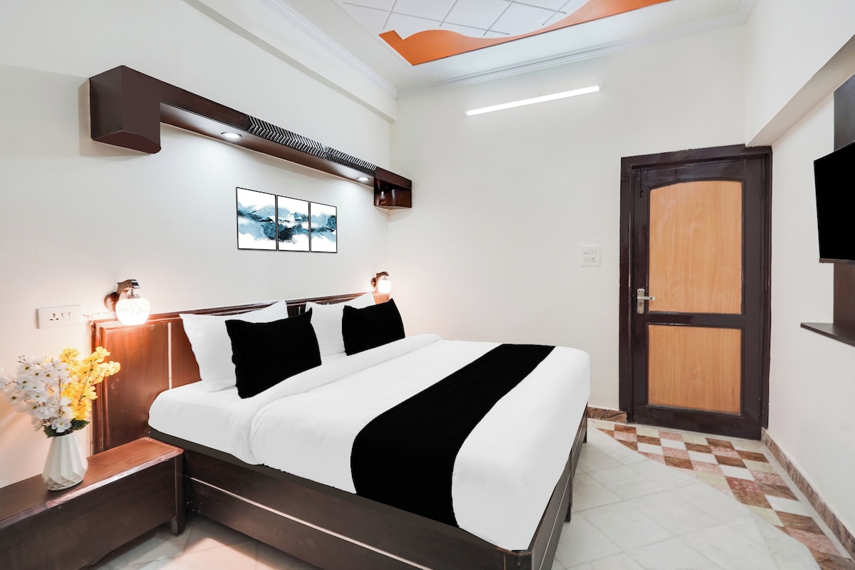 Una habitación de hotel con una cama, mesitas de noche, un televisor montado en la pared, una puerta y una lámpara en el techo.