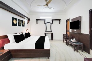 Una habitación de hotel con una cama, un escritorio, una silla, un televisor y un ventilador de techo.
