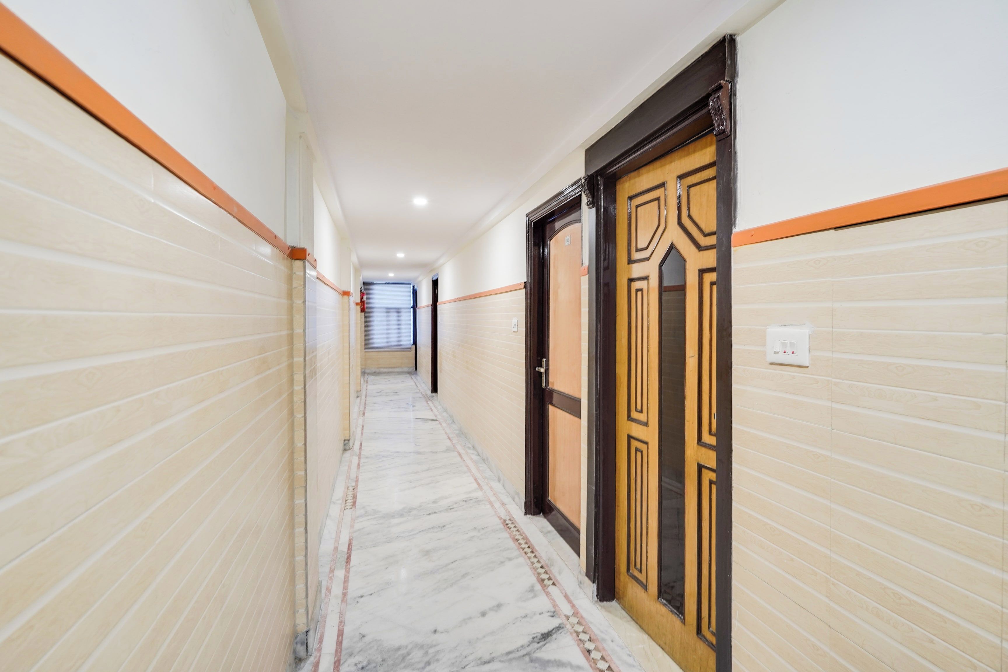 A corridor with tiled walls and a marble floor, leading to a door with a wooden frame and decorative paneling.