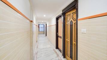 A corridor with tiled walls and a marble floor, leading to a door with a wooden frame and decorative paneling.