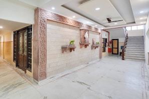 Un pasillo amplio con suelo de mármol, un revestimiento decorativo con intrincados diseños y una puerta con paneles de vidrio.