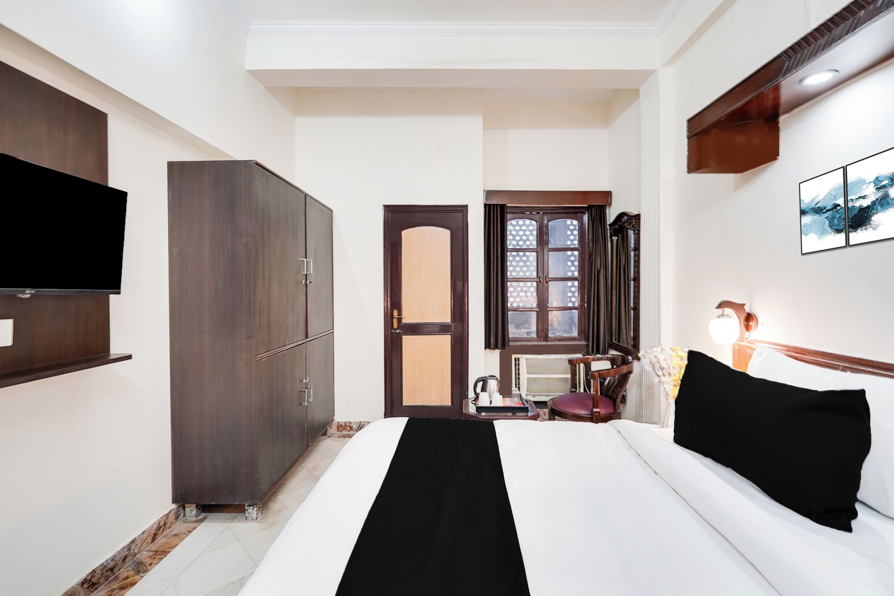 A hotel room with a bed, wardrobe, flat-screen TV, and a window with curtains.