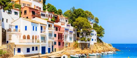 Un pueblo costero con edificios coloridos, un mar azul cristalino y barcos amarrados a la orilla.