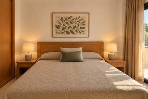 Hotellihuone, jossa on suuri sänky, kaksi yöpöytää valaisimineen, seinällä oleva taideteos kehyksissä ja ikkuna, jossa on verhot.