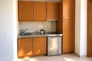 A compact kitchen with wooden cabinets, a stainless steel sink, a coffee maker, and a dishwasher. - Golf Beach Apartment with Pool for 2 (Pals)