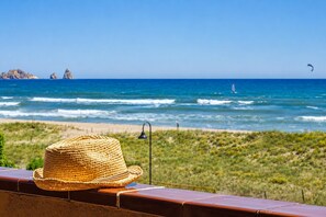 Un barret de palla damunt d'una barana amb vista a una platja, on s'albiren ones i un veler.