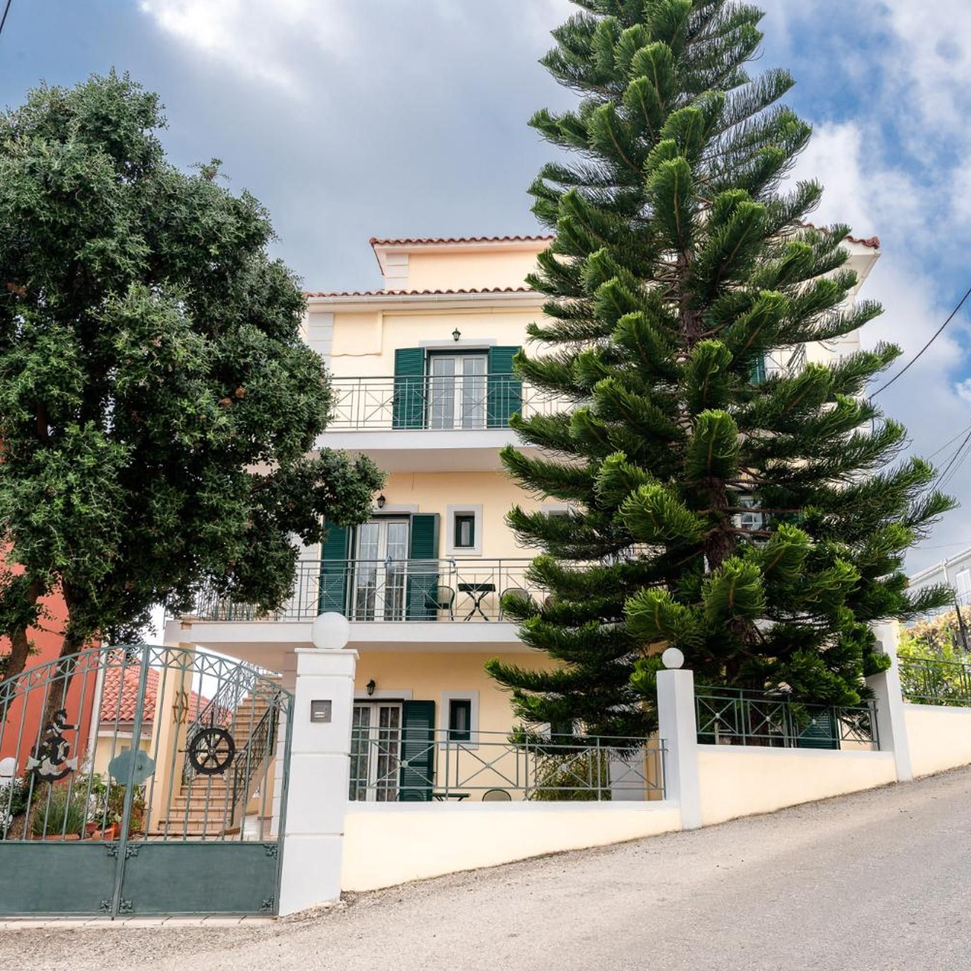 A two-story building with a balcony, a large pine tree in front, and a metal gate with a wheel.