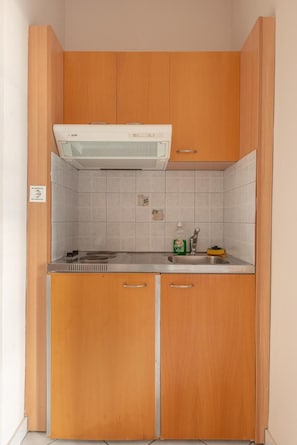 Cocina compacta con armarios de madera, estufa integrada y salpicadero de azulejos.