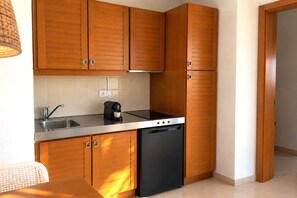 A compact kitchen with wooden cabinets, a stainless steel sink, and a black dishwasher. - Coastal Apartment in Pals for 2 (Pals)