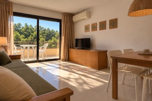 A hotel room with a balcony, a sofa, a dining table with chairs, a TV on a wooden cabinet, and artwork on the wall. - Coastal Family Apartment with Pool (Pals)