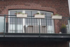 A balcony with three flower boxes, a metal railing, and a brick building in the background. - Holiday apartment with 1 bedroom (Otterndorf)