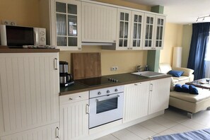 Une cuisine compacte avec des meubles blancs, un four encastré, un four à micro-ondes et une machine à café.
