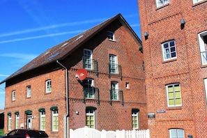A red brick building with multiple windows and a white picket fence. - Holiday apartment with 1 bedroom (Otterndorf)
