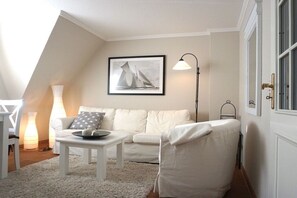 A white room with a white sofa, a small table, a lamp, and a framed picture of a sailboat on the wall. - in the country house Arnfried, upper floor (Wenningstedt)