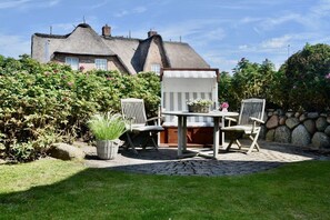 Une terrasse avec une table et des chaises, entourée d’un mur de pierre et d’une haie.
