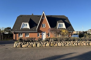 A two-story house with a stone wall in front, a brick facade, and a sloped roof. - in the country house Arnfried, upper floor (Wenningstedt)