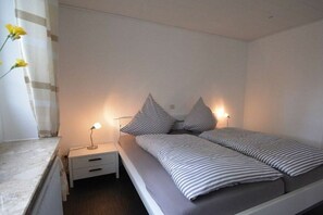 Ein Einzelbett mit gestreifter Bettwäsche, ein Nachttisch mit Lampe und ein Heizkörper.