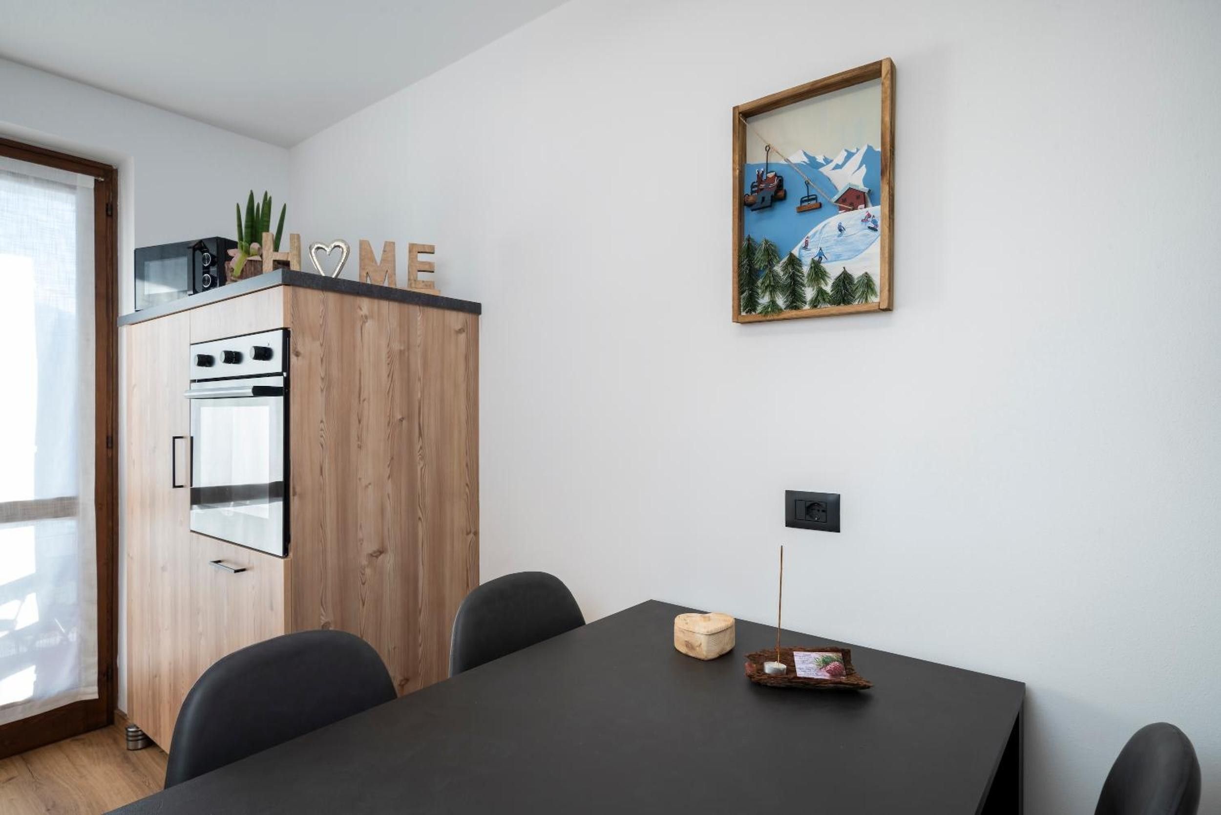 Une cuisine moderne avec des meubles en bois, une table à manger noire et un tableau encadré accroché au mur.