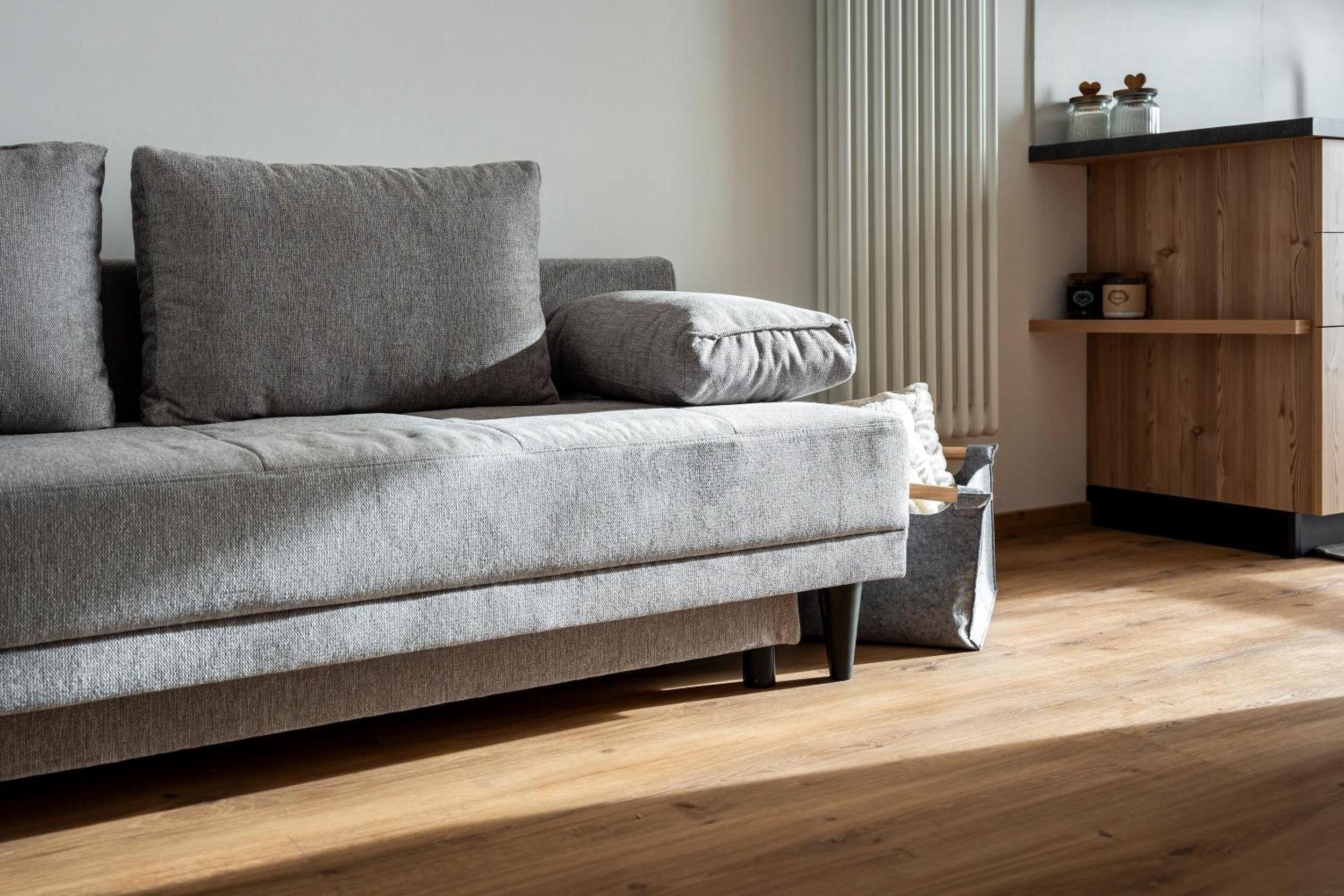 Ein graues Sofa mit vielen Kissen, Holzboden und eine Holzkommode mit Dekoration.
