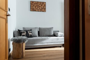 Un sofá gris con dos almohadones decorativos, un taburete de madera con un cubrefrío de piel y una obra de arte colgada en la pared.