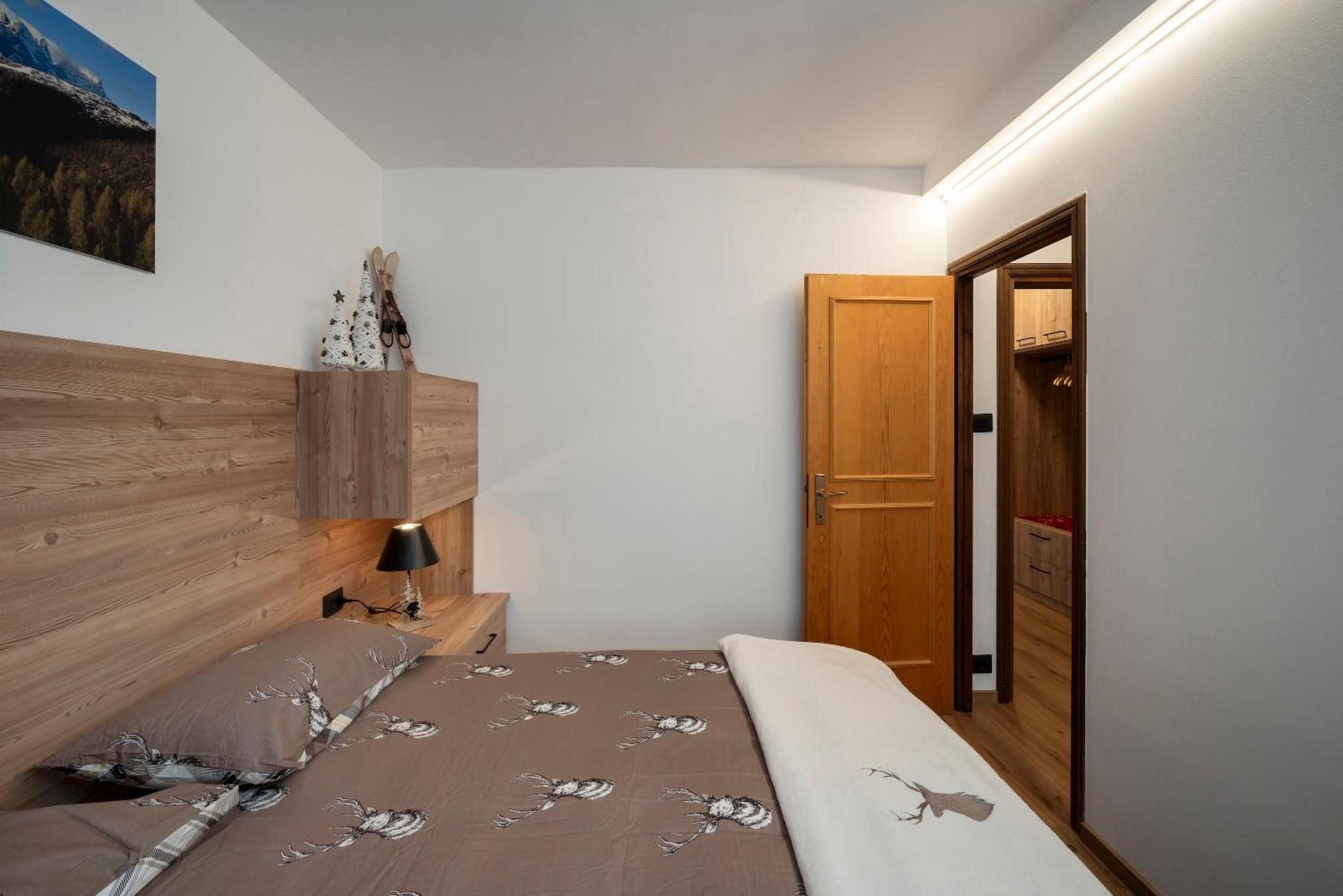 A bedroom with a wooden headboard, a bed with patterned bedding, a nightstand with a lamp, and a wardrobe with a mirror.