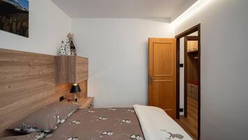 A bedroom with a wooden headboard, a bed with patterned bedding, a nightstand with a lamp, and a wardrobe with a mirror.