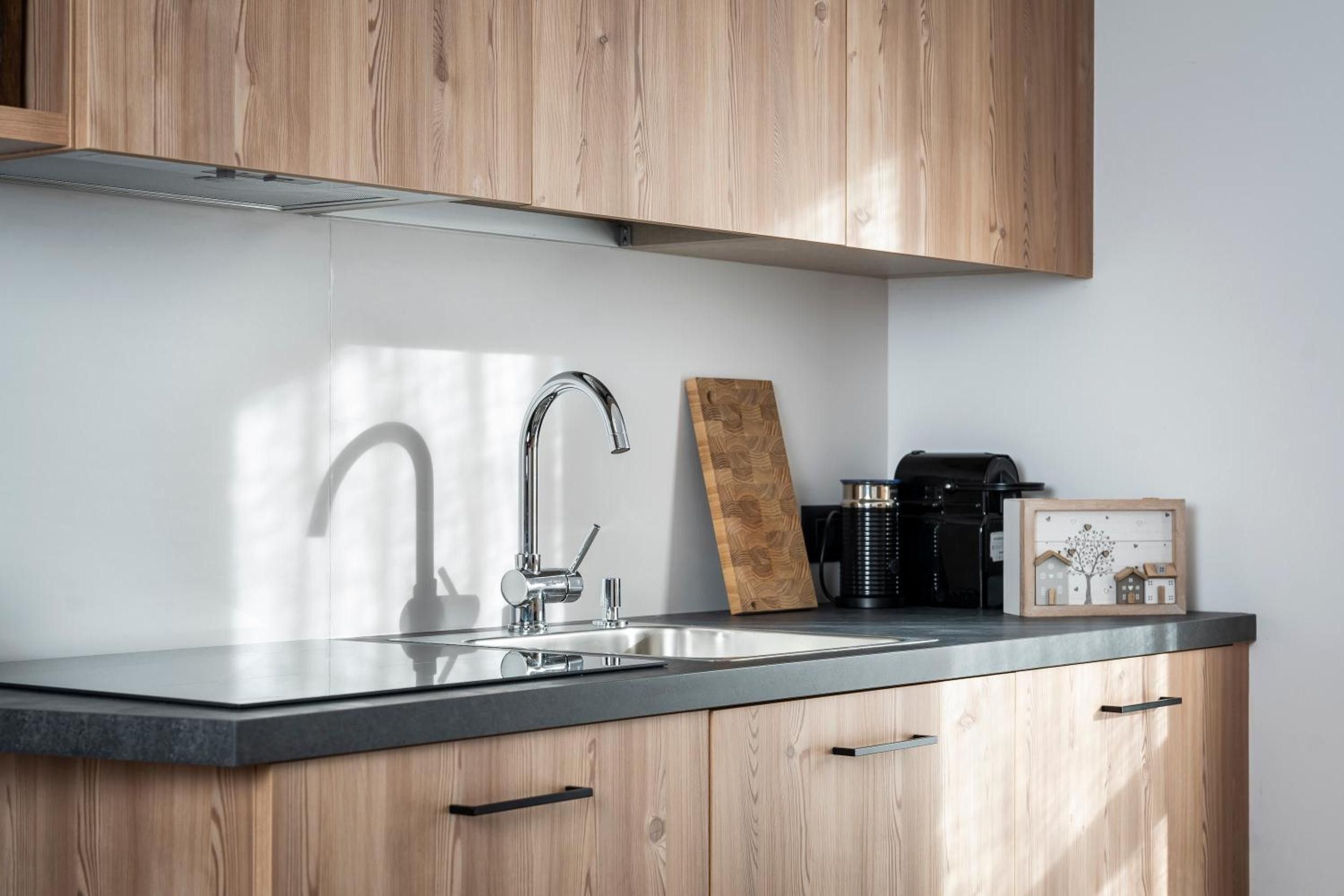 A modern kitchen with a stainless steel sink, wooden cabinets, and a coffee maker.