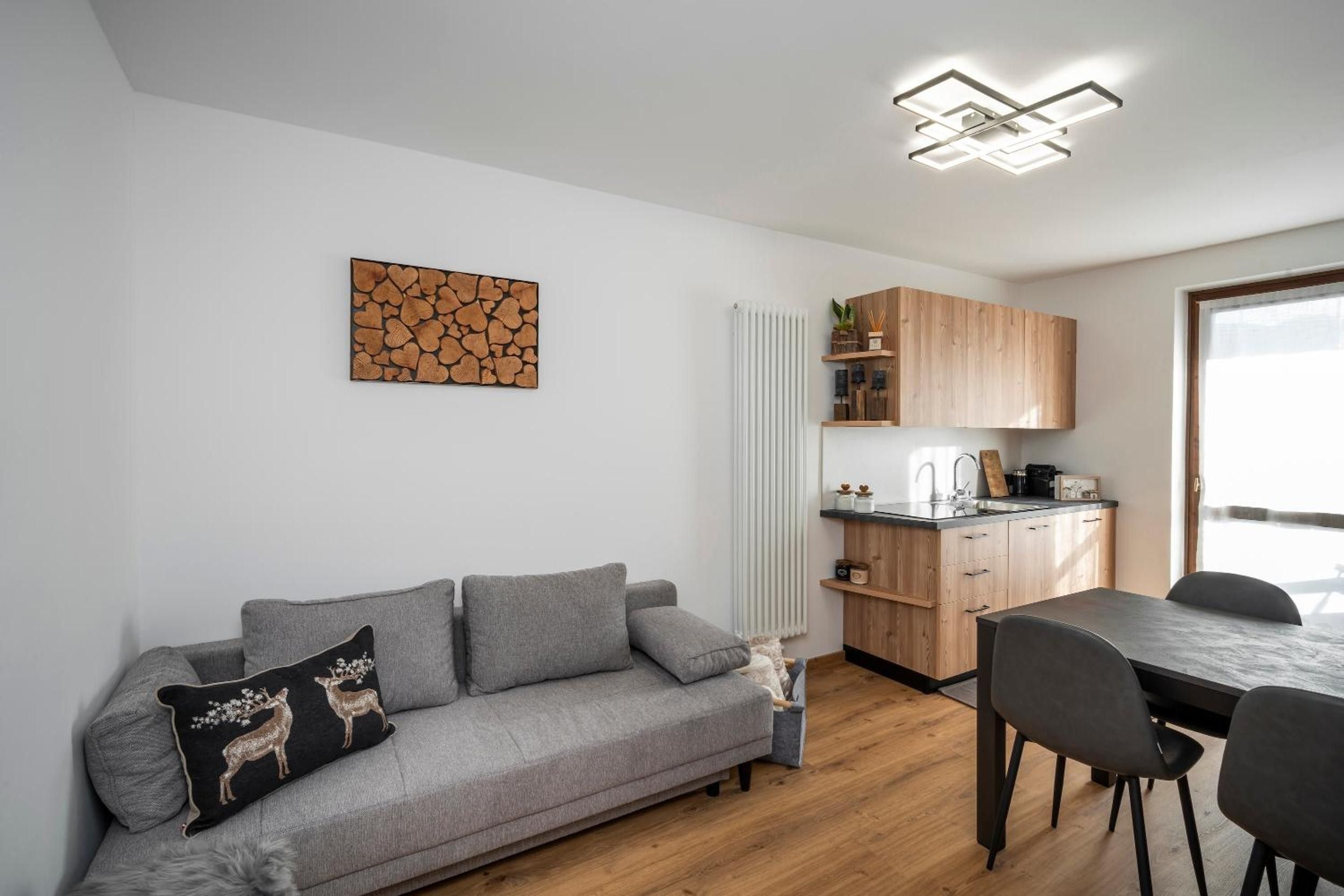 A modern living space with a grey sofa, a dining table with chairs, a kitchen area, and a ceiling light fixture.