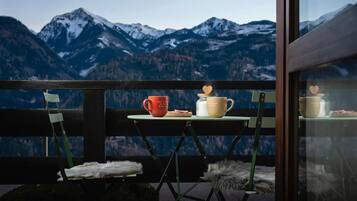 Un balcon avec une table dressée pour deux personnes, offrant une vue sur des montagnes enneigées.