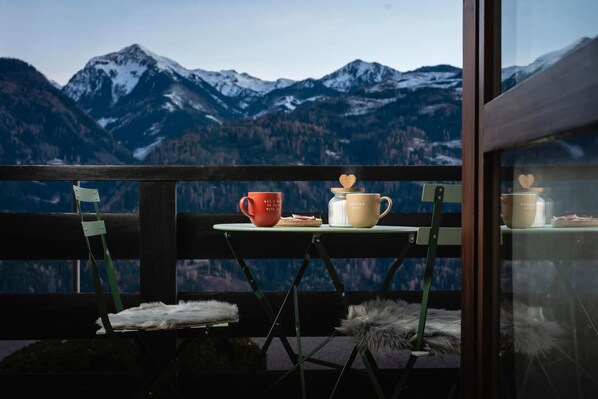 A balcony with a table set for two, overlooking snow-capped mountains.
