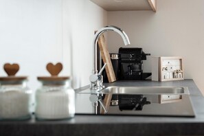 A kitchen with a stainless steel sink, a coffee machine, and jars with heart-shaped lids.