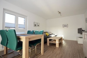 A modern living room with a dining table, chairs, a sofa, and a television. - Holiday apartment with 1 bedroom (Norden)