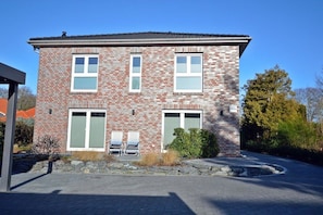 A two-story brick house with a garage, a covered patio, and a small garden area. - Holiday apartment with 1 bedroom (Norden)