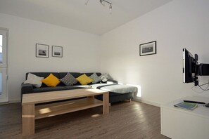 A modern living room with a sofa, a coffee table, and a flat-screen TV mounted on the wall. - Holiday apartment with 1 bedroom (Norden)