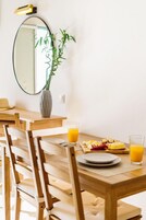 Un comedor con mesas y sillas de madera, un florero con plantas verdes y opciones para el desayuno, como huevos y fruta.