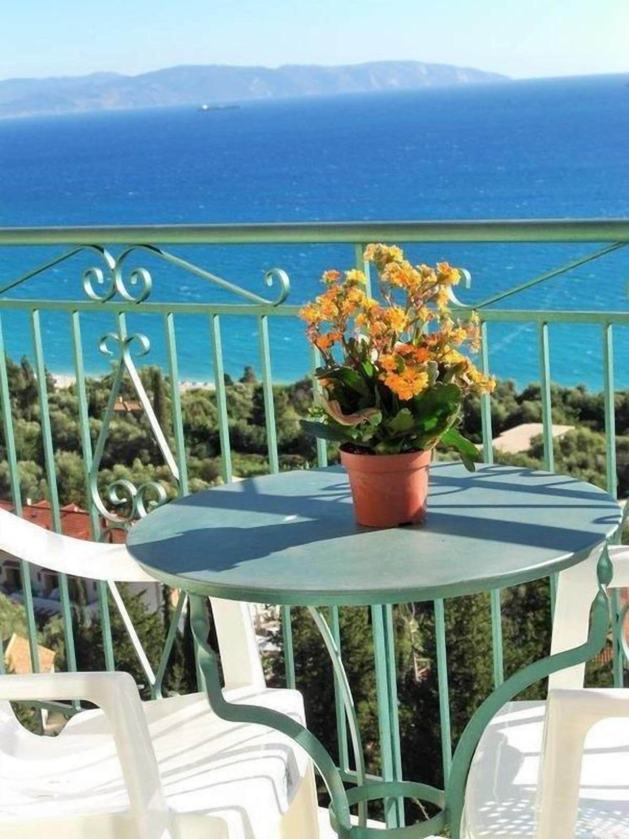A balcony with a table and chairs, a potted plant, and a view of the sea.