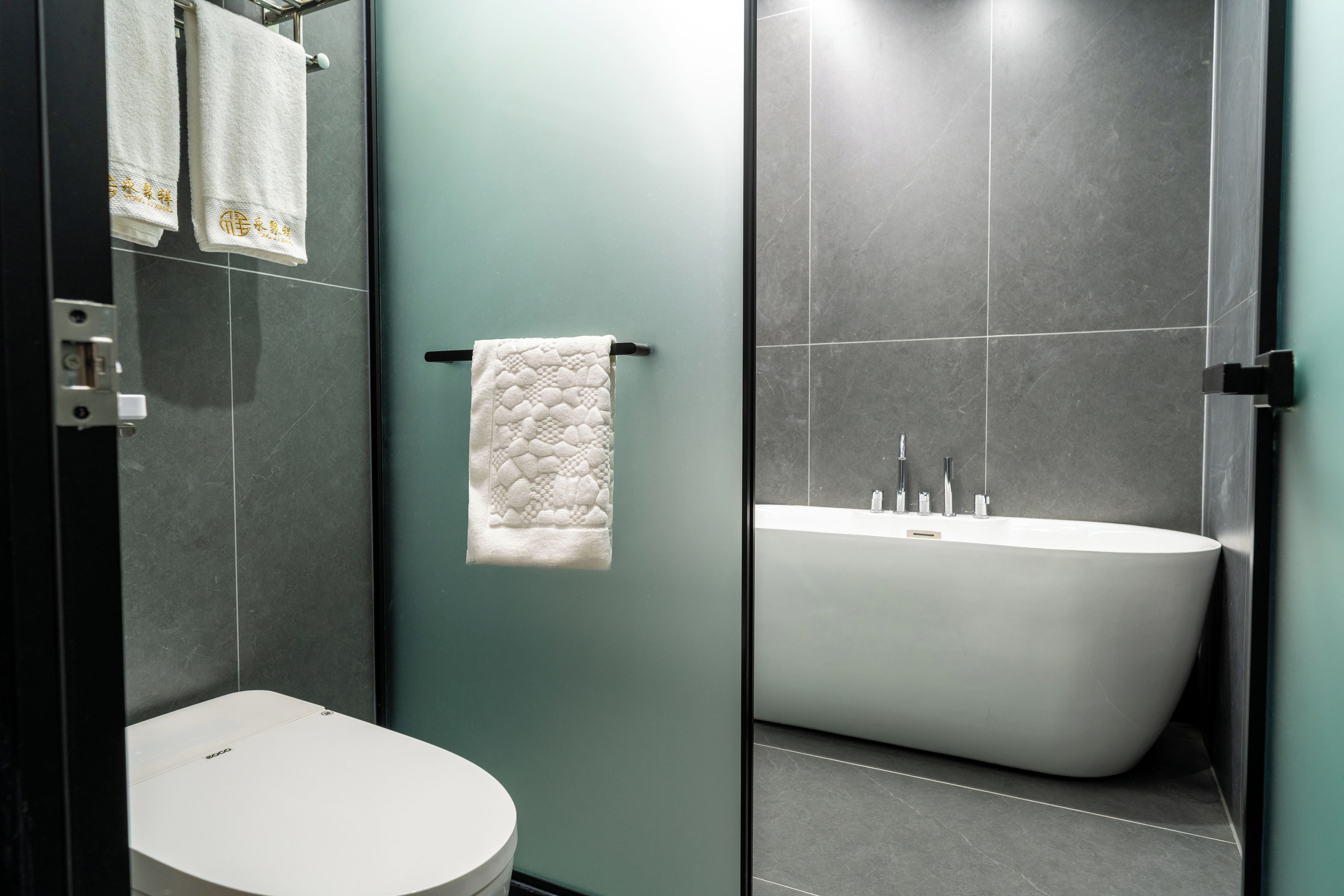 Un baño moderno con inodoro, un perchero con dos toallas y una bañera independiente.