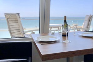 Ein Esstisch mit einer Weinflasche und Gläsern, mit Blick auf einen Strand.