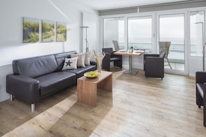 Ein modernes Wohnzimmer mit einem grauen Sofa, einem Holztisch und einem Essbereich mit Stühlen.