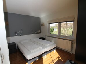 Ein Schlafzimmer mit Doppelbett, Nachttischen, einem Fenster mit Blick auf Grünflächen und einer Heizung.