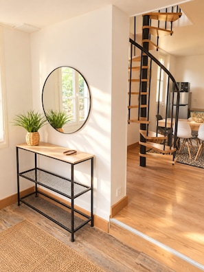 Ein modernes Interieur mit einer Wendeltreppe, einem runden Spiegel und einem Holzkonsolentisch mit einer Pflanze.